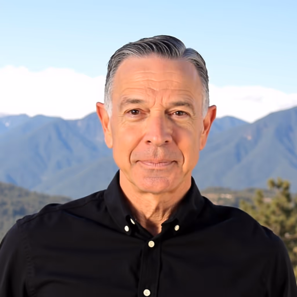 Middle-aged man with gray hair wearing a black button-up shirt with mountains in the background.