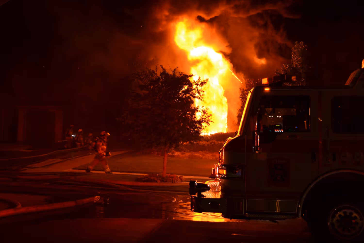 Frisco firefighters battling a large house fire at night with flames rising behind a fire engine