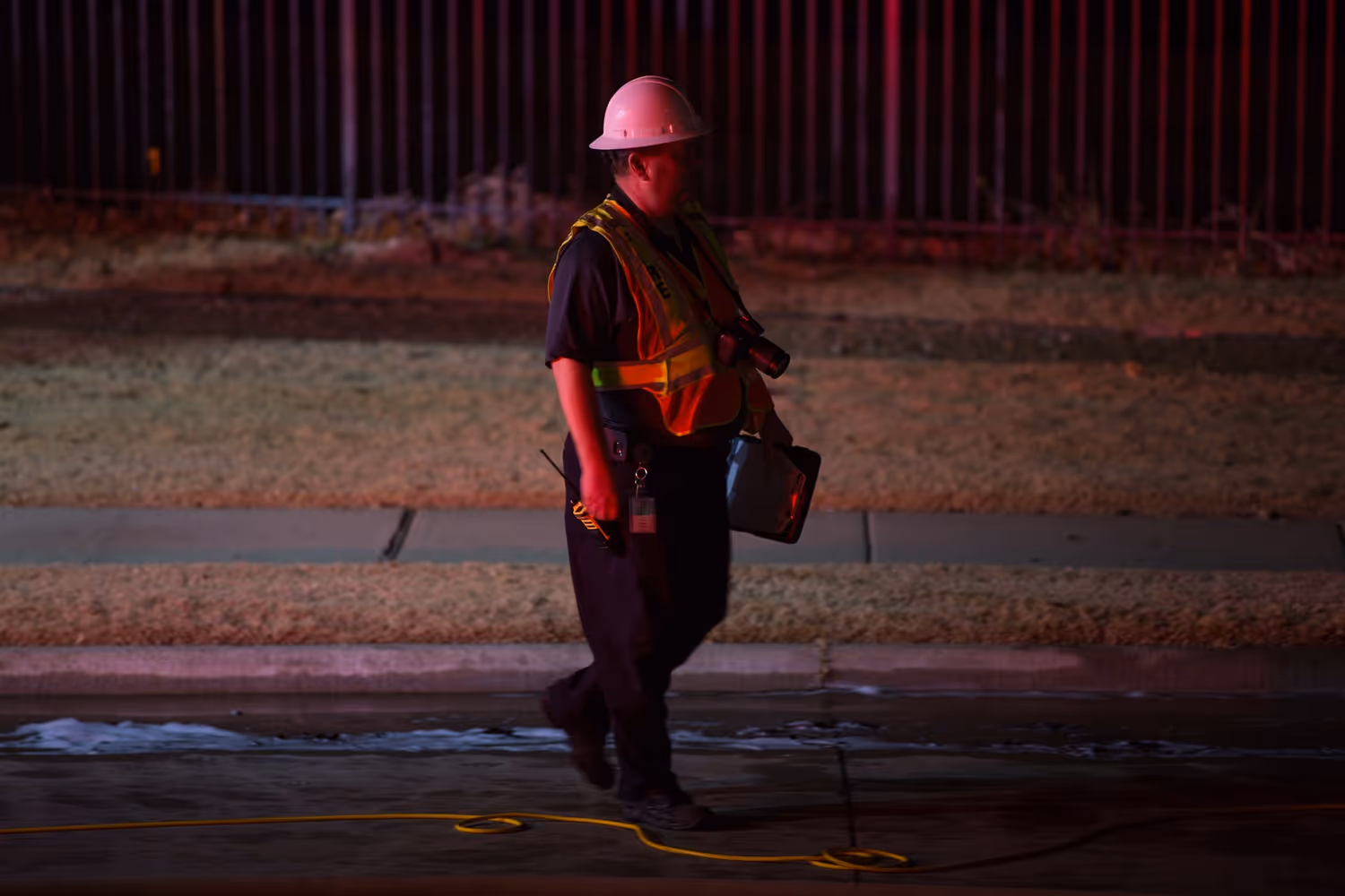 Fire department official wearing a helmet and safety vest walking at night with equipment after a fire incident