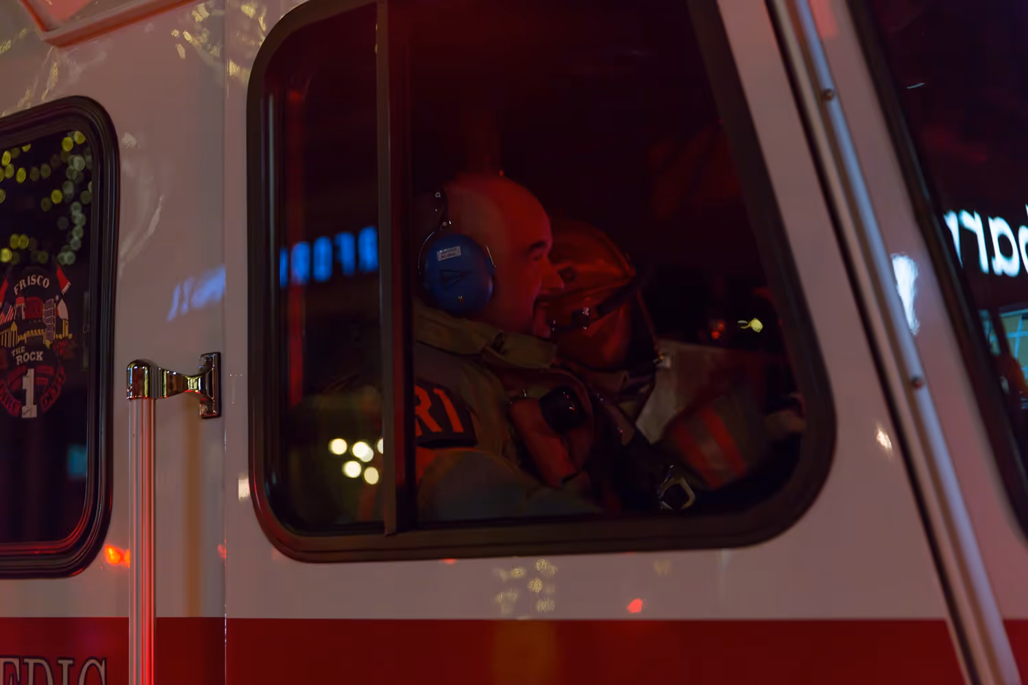 Close-up of a firefighter inside a fire apparatus wearing a headset and communicating during a nighttime emergency call