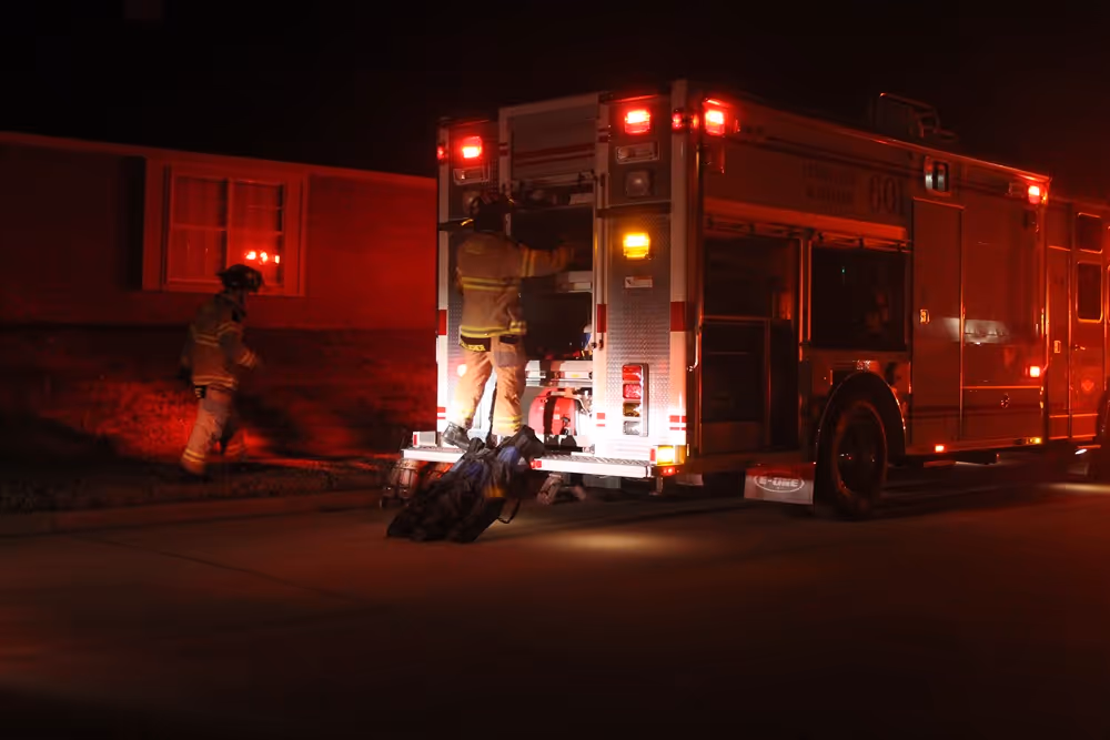 Frisco firefighters working at the back of a fire engine during a nighttime emergency, illuminated by red emergency lights in a residential neighborhood