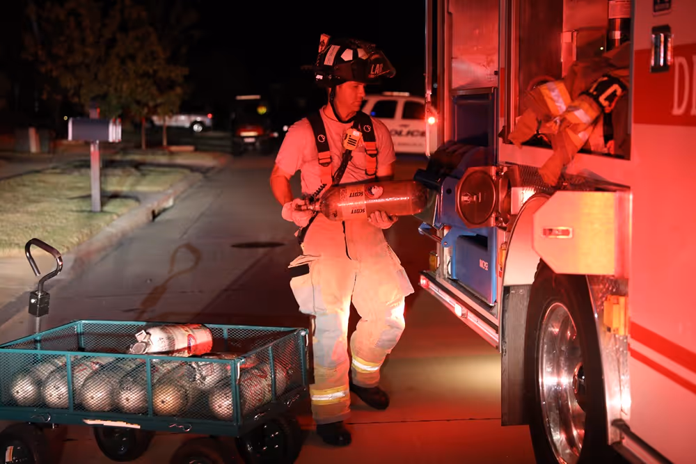 Frisco firefighter transferring oxygen tanks from a cart into a fire truck during a nighttime emergency response