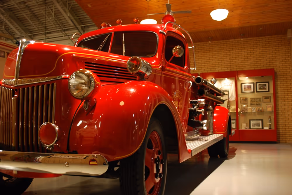 Close-up of a vintage red fire truck on display inside a museum with framed memorabilia in the background