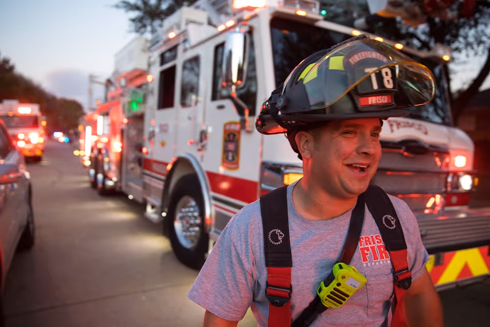 Frisco firefighter smiling in front of a fire truck during an emergency response at dusk