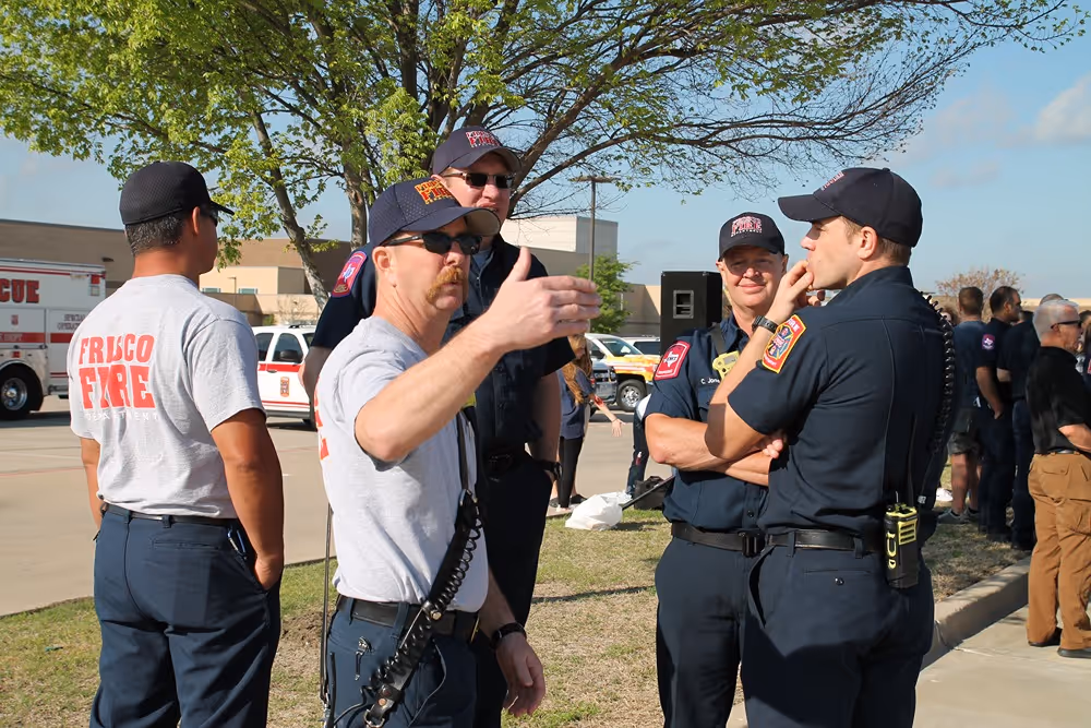 Group of Frisco firefighters in uniform standing outside and talking during a sunny community or department event