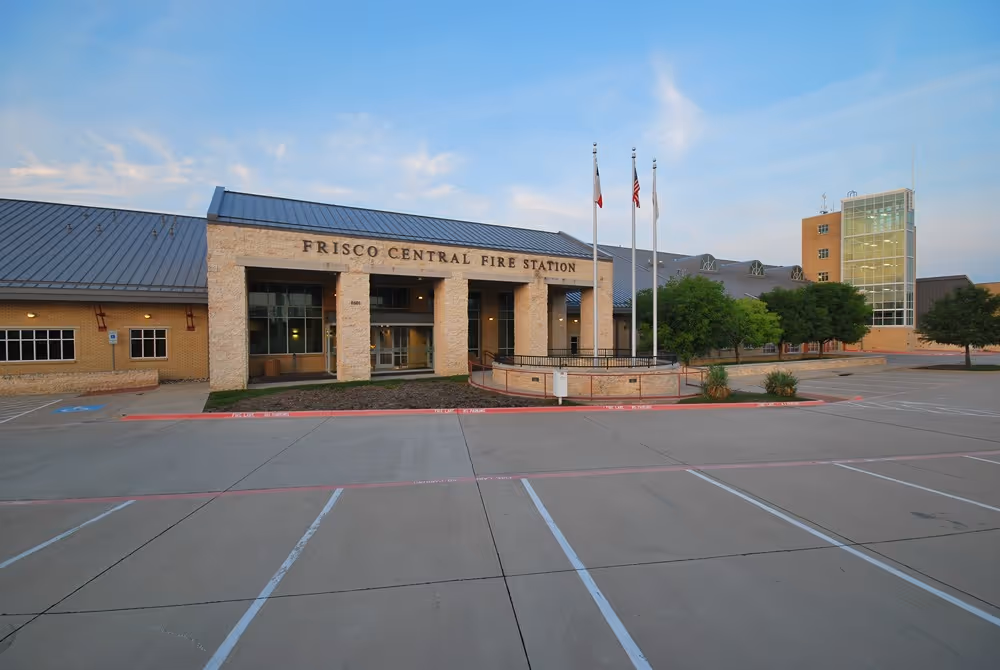 Frisco Central Fire Station building with three flags in front, photographed at dusk in an empty parking lot