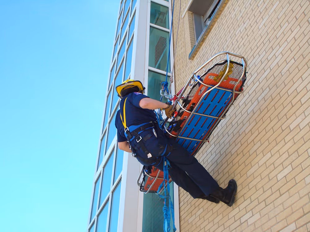 Firefighter performing a high-angle rescue training drill on the side of a building using ropes and a stretcher