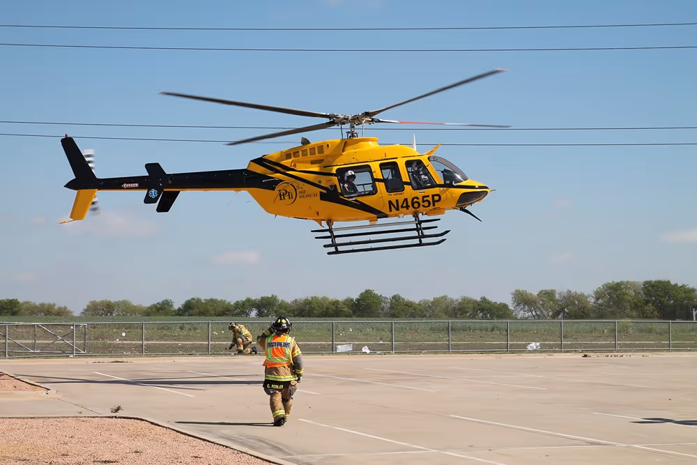 Frisco firefighter walking toward a yellow emergency medical helicopter preparing to take off from a landing zone