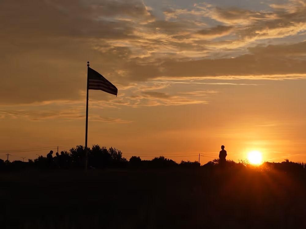 Silhouette of an American flag waving at sunset with a dramatic sky in the background