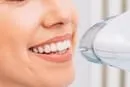 A woman is smiling while using a hair dryer.