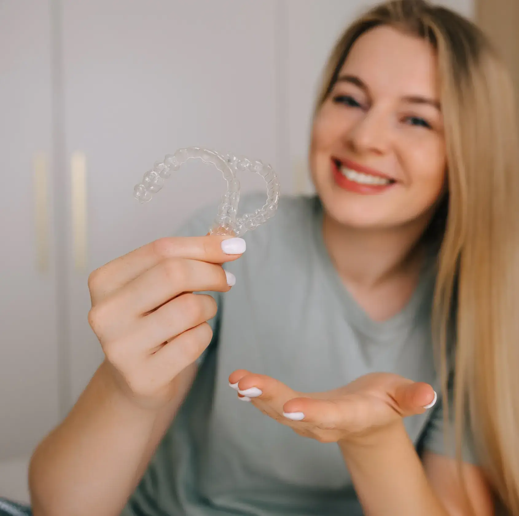 Smiling woman holding two clear Invisalign aligners in front of her.
