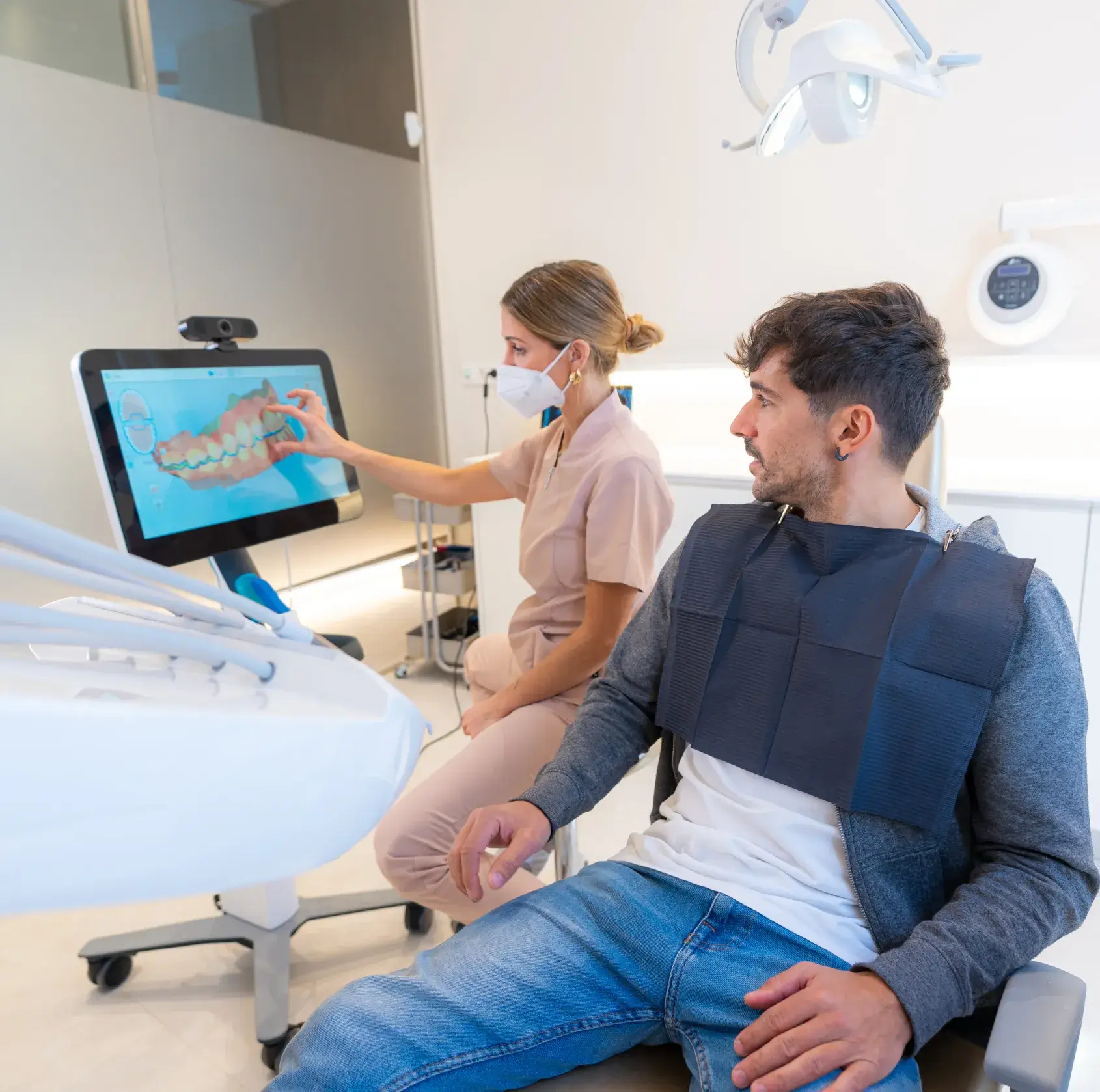 Dentist wearing a mask explaining a dental scan on a screen to a male patient seated in a dental chair.
