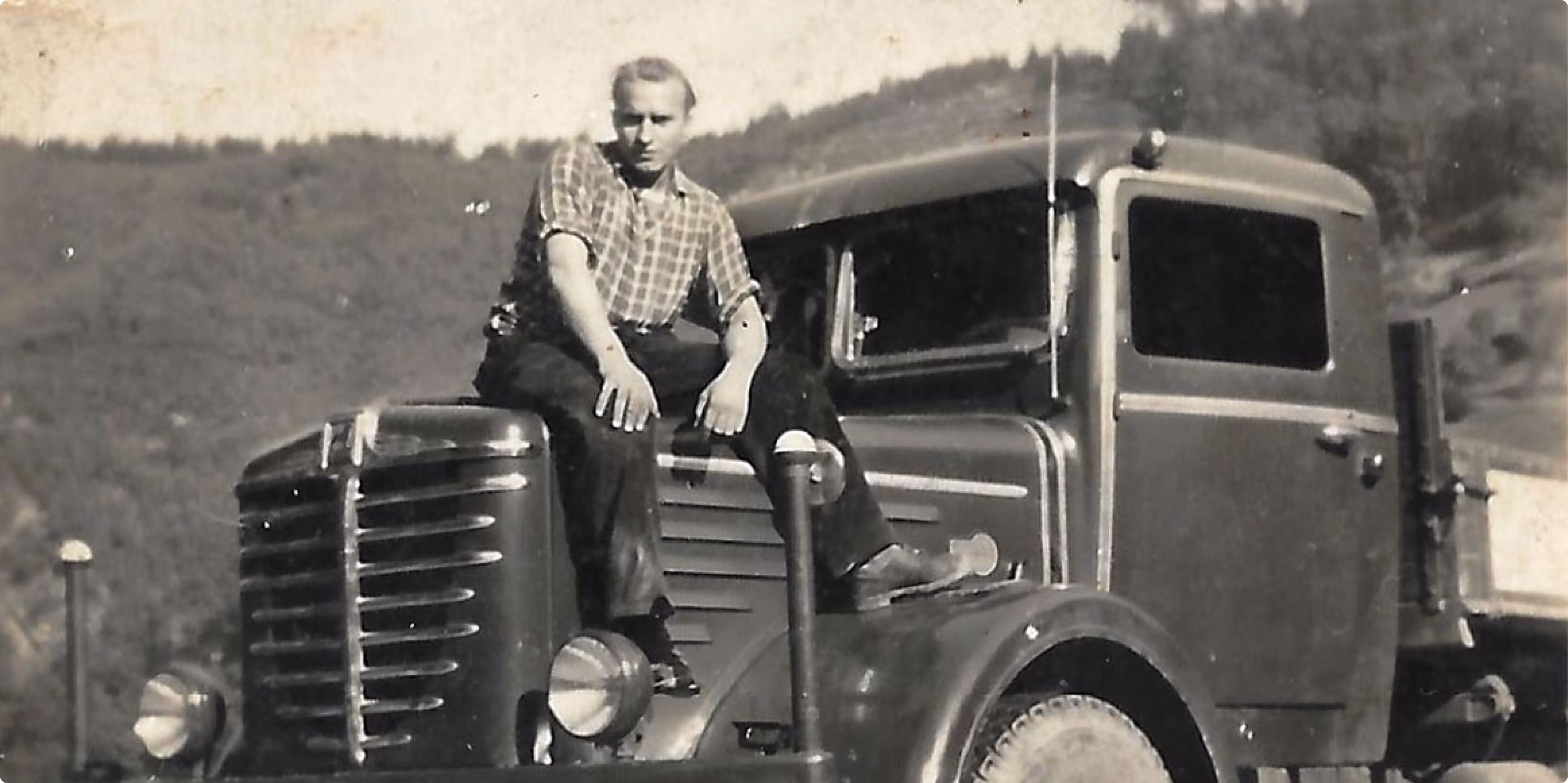 Historisches Schwarzweißfoto eines Mannes auf einem Oldtimer-LKW, symbolisiert die Unternehmensgeschichte seit 1923