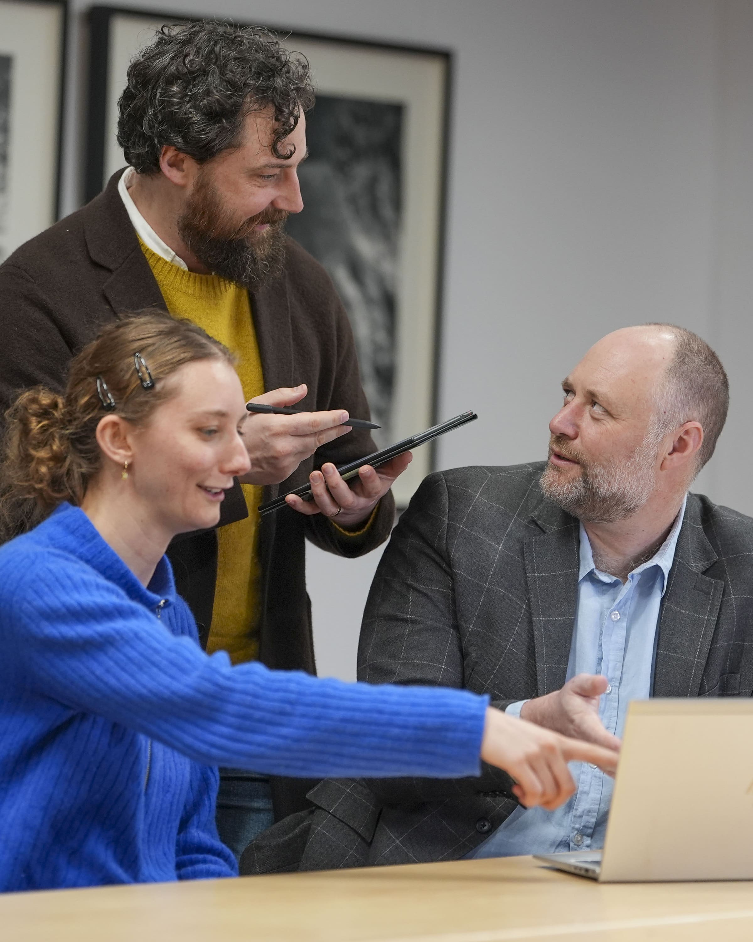 The founder of the AI training company, Shaun Davies, instructs a standing man and a sitting woman on the use of AI in front of a laptop. 