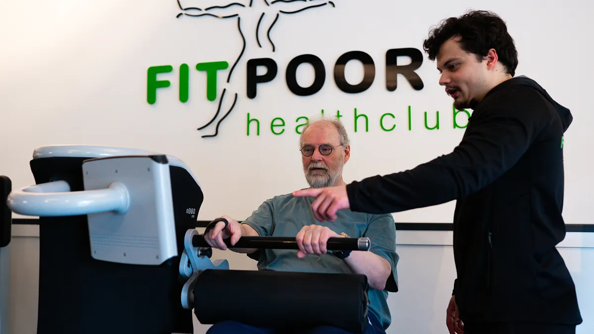 Een trainer van Fitpoort Healthclub geeft uitleg over een Egym apparaat.