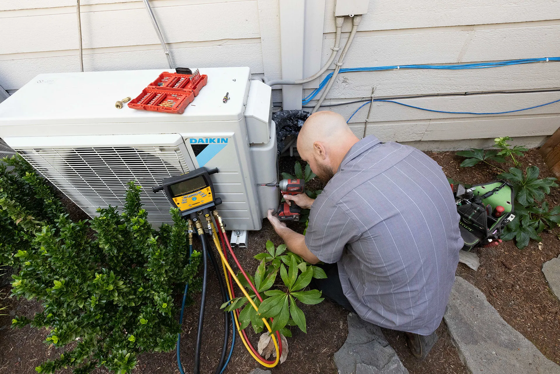 HVAC technician using a power drill to secure a part of a heat pump on exterior of a home