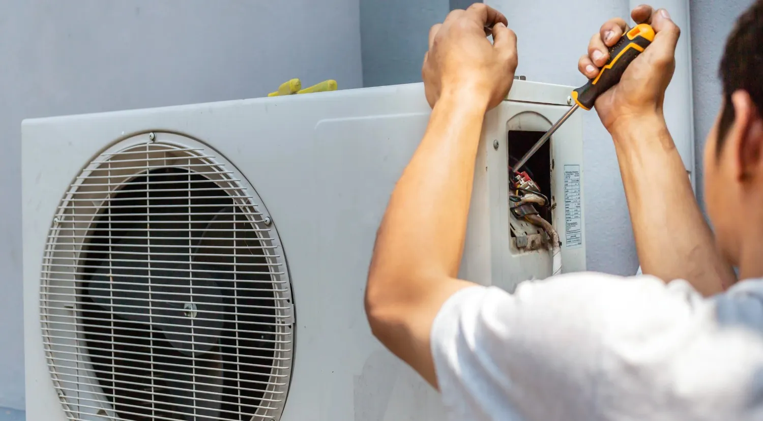 A close-up shows hands working with tools on the top of a white outdoor air conditioning unit