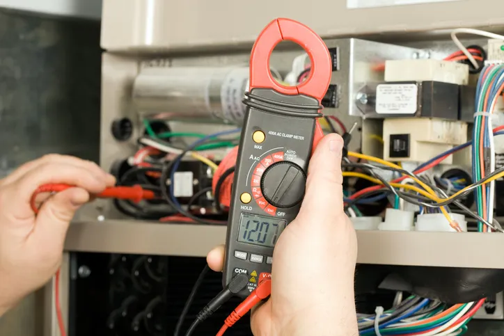 Hands using a clamp meter to measure electrical current in an HVAC unit.