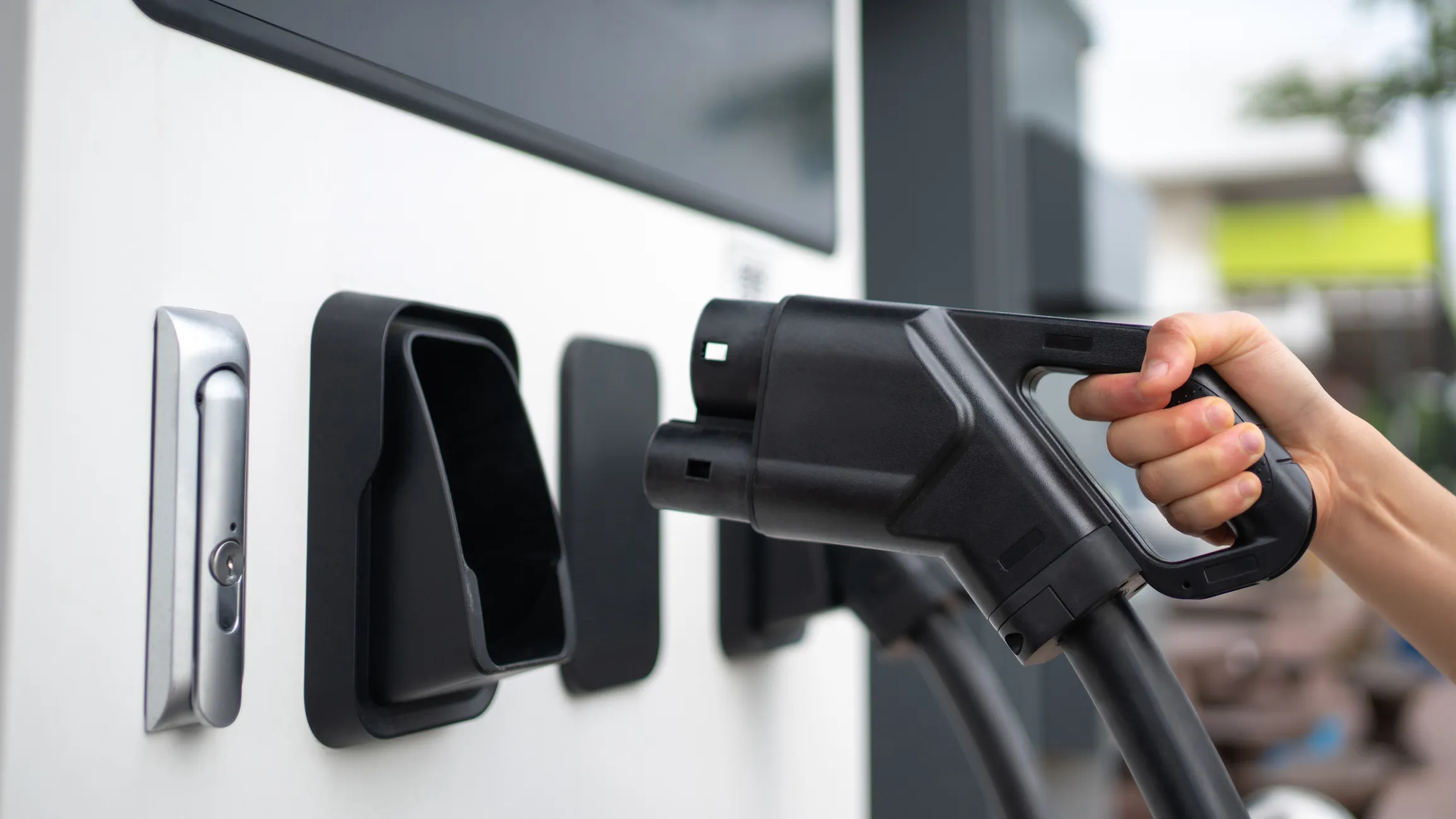 Close-up of a person gripping a CCS or CHAdeMO EV charging plug at a rapid charging station.