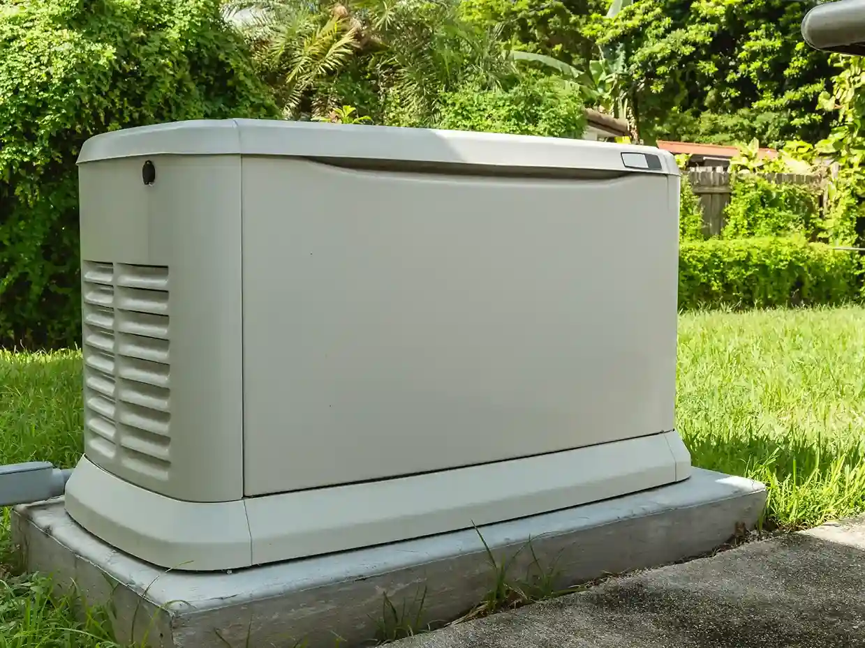 Residential standby generator unit installed on a concrete pad in a lush backyard.