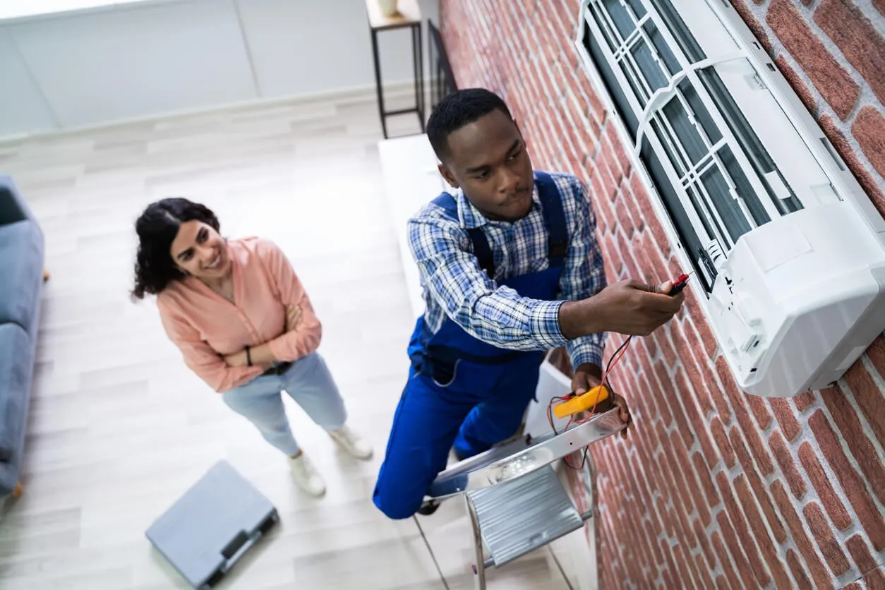 Technician checking indoor AC unit, customer smiles.