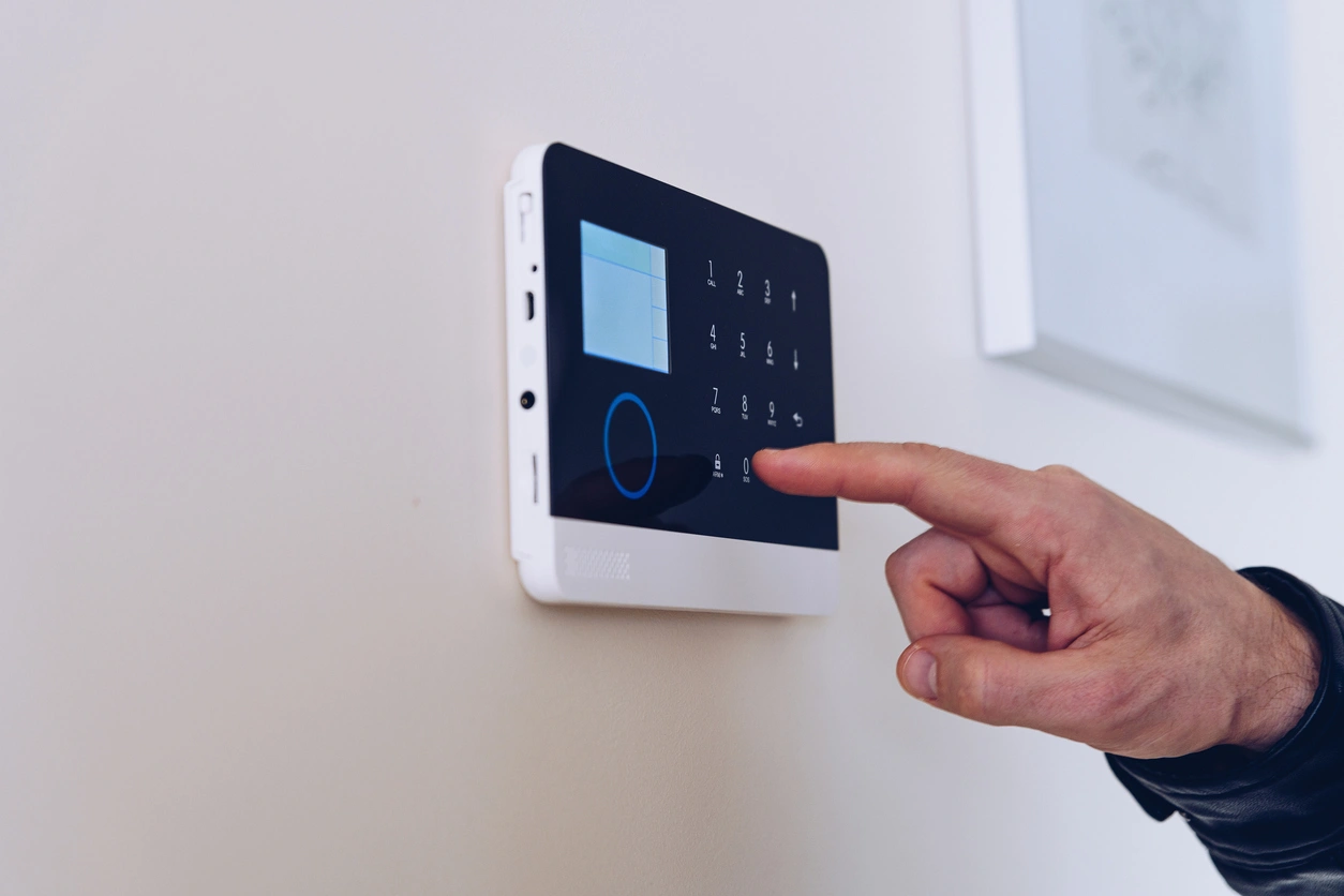 A hand interacts with a sleek, wall-mounted digital security keypad on a neutral wall.