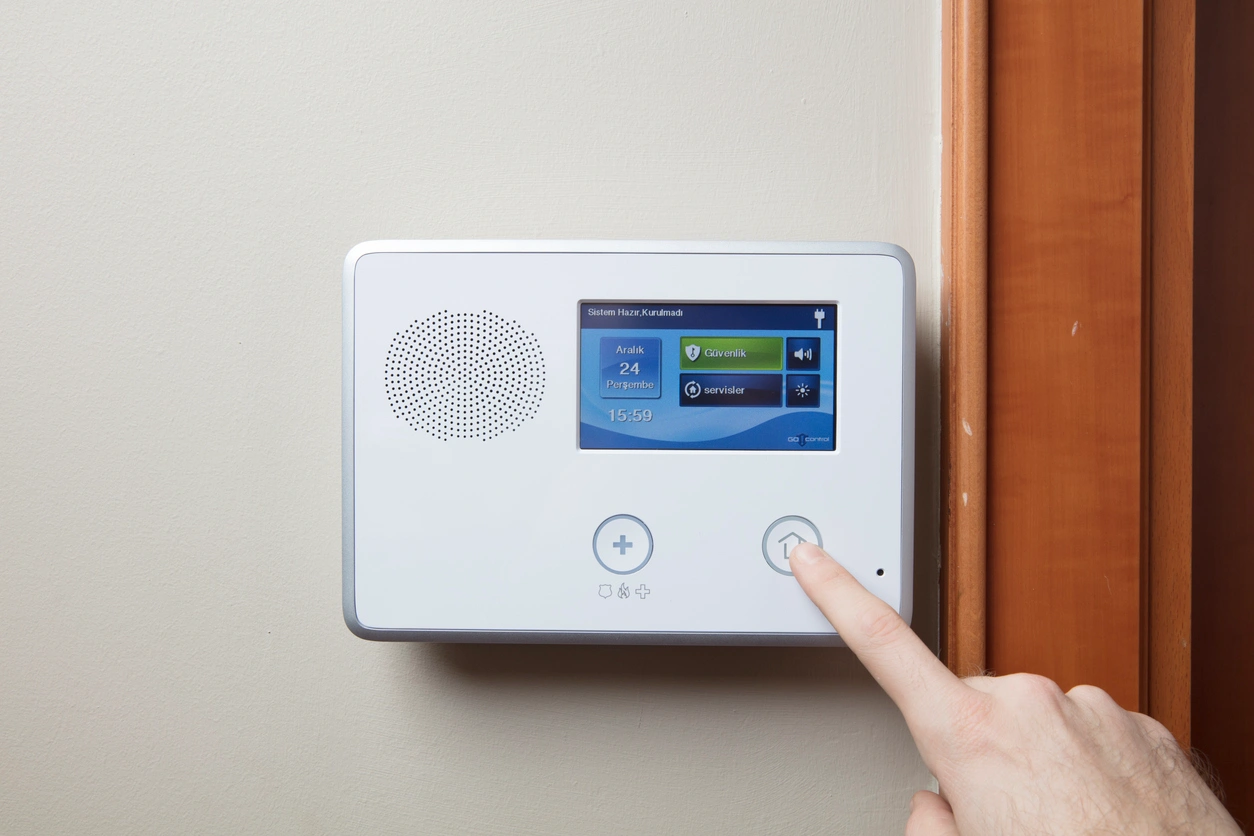 A hand interacts with a white wall-mounted home alarm control panel