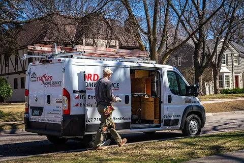 Stafford Home Service van parked on residential street, technician preparing for structured wiring installation, emphasizing HVAC and home entertainment solutions.