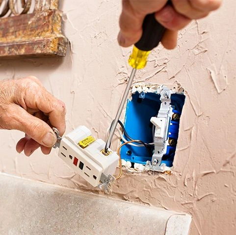 Electrician installing a GFCI outlet in a residential wall, emphasizing electrical safety and compliance.