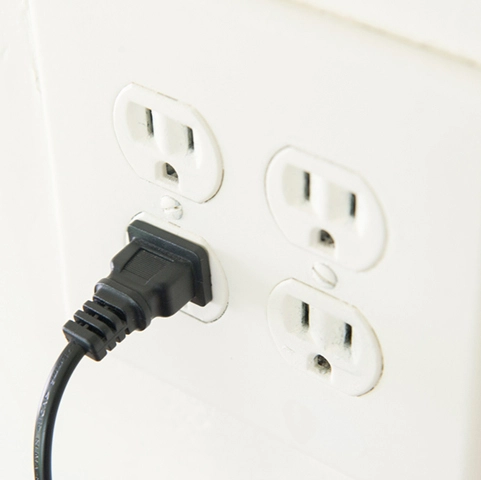 Electrical outlet with a black power cord plugged in, illustrating isolated ground installation to reduce electromagnetic interference for sensitive electronics.