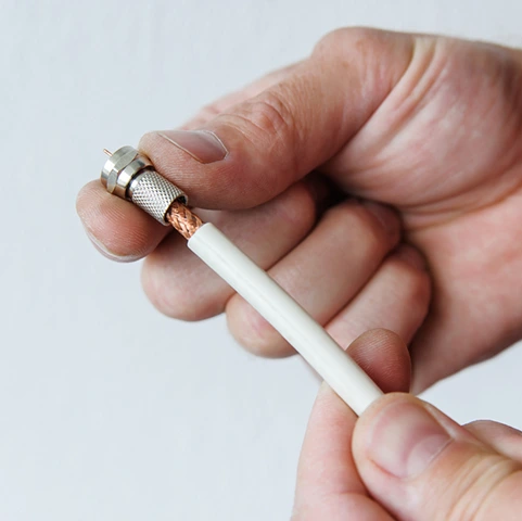 Hand holding a low-voltage wiring cable, showcasing a coaxial connector, relevant to residential electrical services for communication and entertainment systems.