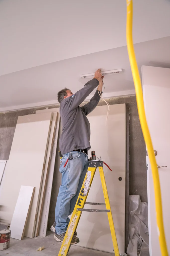 Electrician installing ceiling light fixture on ladder in residential setting, emphasizing electrical wiring services in Minneapolis, MN.