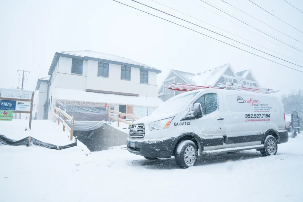 Stafford Home Service van parked in snowy conditions outside a residential construction site, emphasizing winter electrical service readiness for holiday lighting installations.