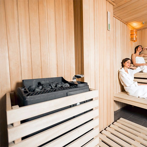 Sauna interior with wooden walls, featuring a heater, two women relaxing on benches, emphasizing sauna wiring and electrical safety in residential installations by Stafford Home Service.