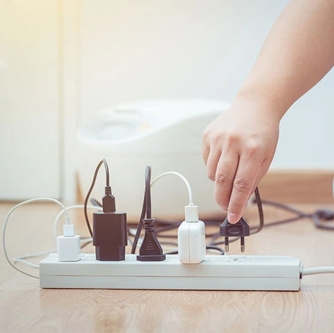 Hand plugging in a device to a power strip, emphasizing surge protection for home electronics and appliances.