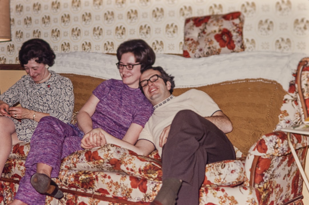 Cozy living room scene with three people sitting on a floral-patterned couch, two smiling while enjoying each other's company, reflecting warmth and comfort.