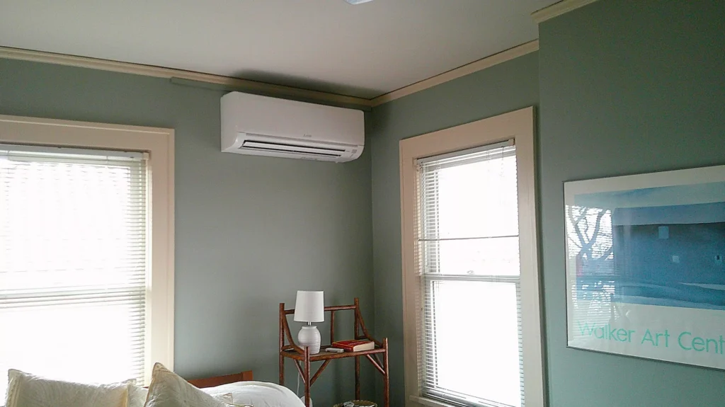 Ductless heat pump wall unit installed in a room, providing efficient heating and cooling, with a modern design and nearby window for natural light.