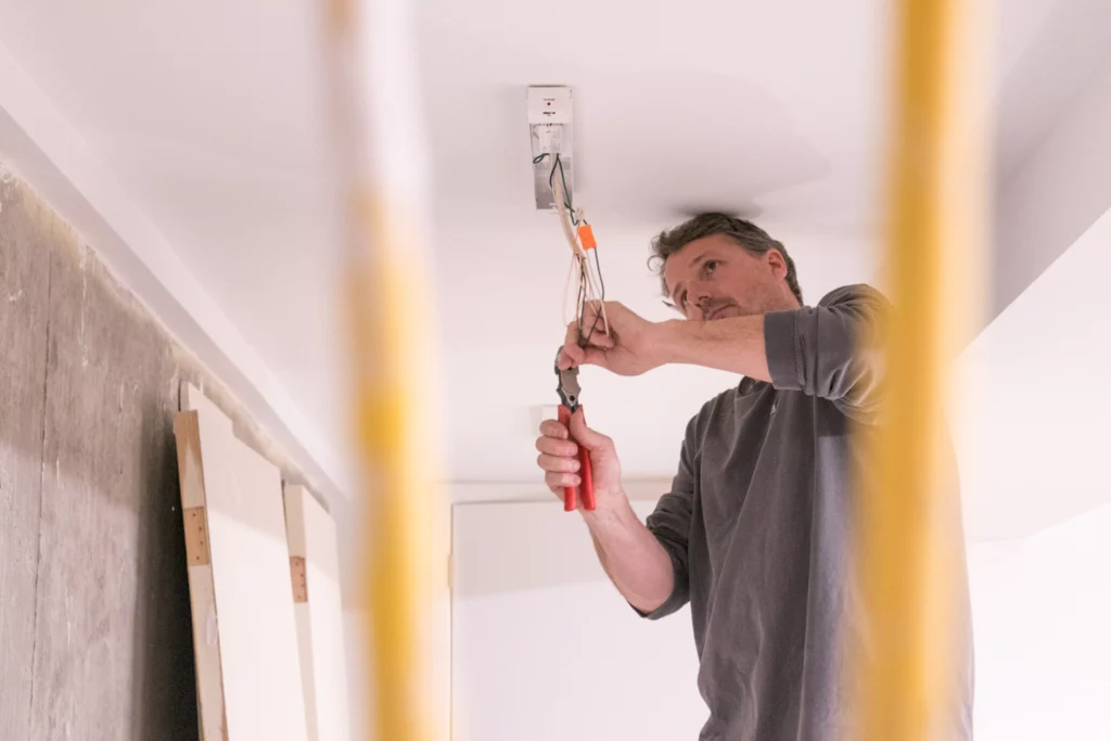 Man installing electrical fixture using pliers during home renovation, highlighting residential electrical services in Mendota Heights, MN.