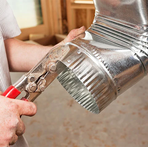 Person using metal snips to cut ductwork for HVAC installation, emphasizing ductwork design and fabrication services in Minneapolis, MN.
