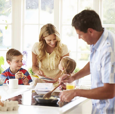 Family enjoying time in a kitchen, with a mother engaging with her children while a father cooks, illustrating the importance of indoor air quality in a home environment.