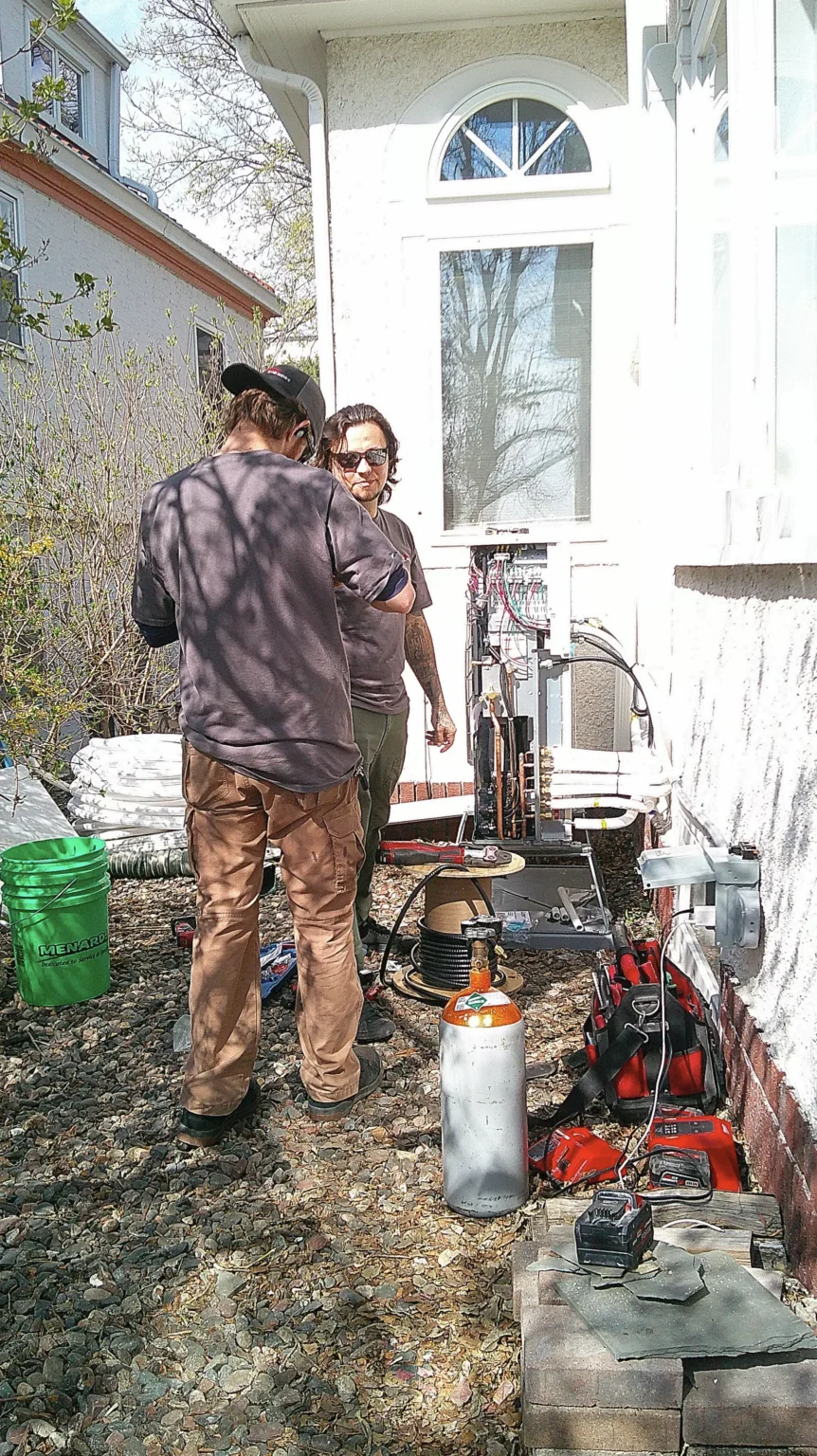 Technicians servicing a heat pump unit outside a residential building in Edina, MN, with tools and equipment for HVAC maintenance.