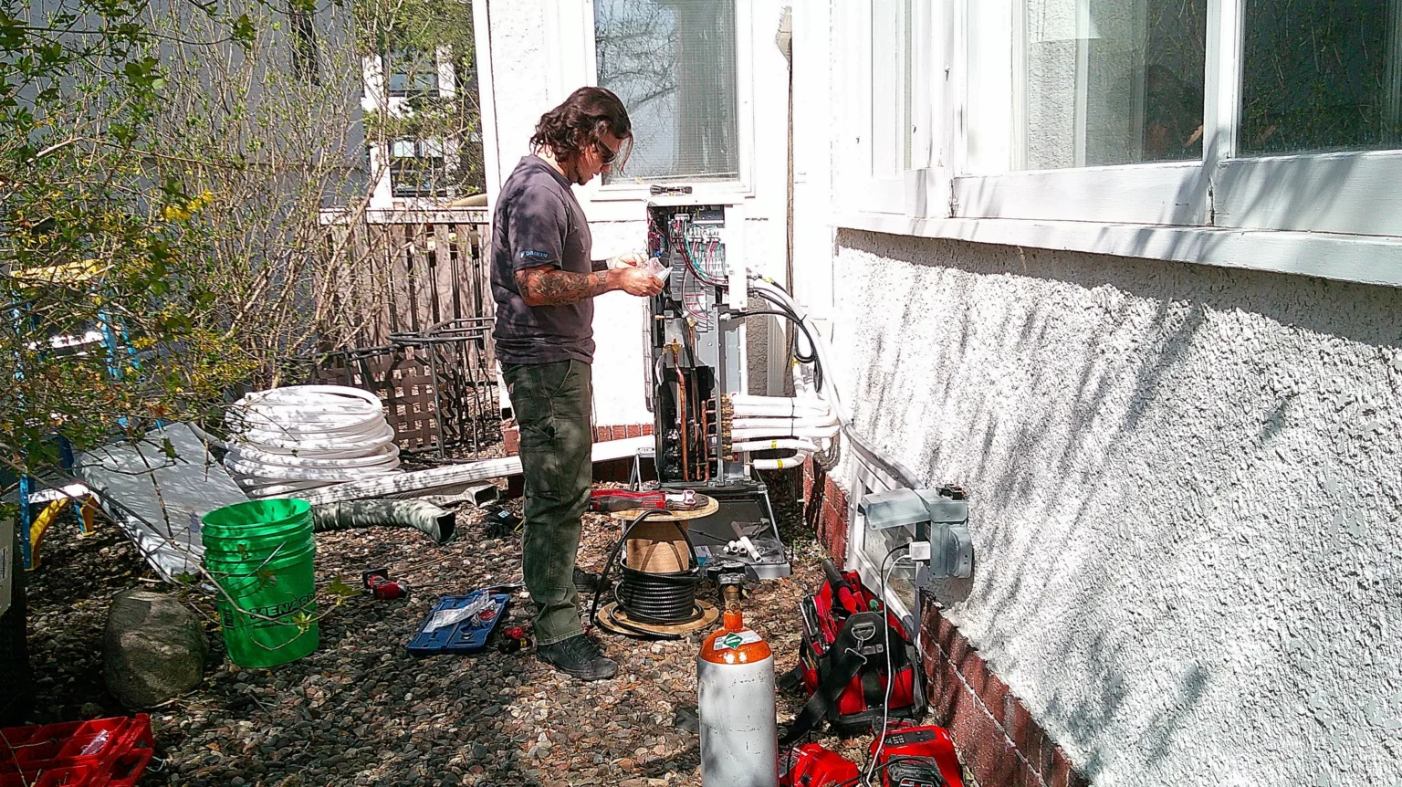Technician installing a heat pump system outdoors in Golden Valley, MN, surrounded by tools and equipment for HVAC service.