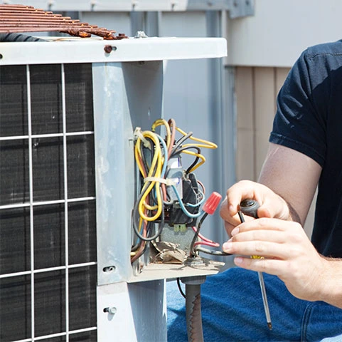 Technician repairing HVAC system with exposed wiring and tools, emphasizing HVAC systems repairs and maintenance services in Minneapolis, MN.