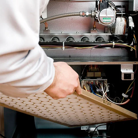 Technician replacing air filter in HVAC system during scheduled preventative maintenance for heating and cooling efficiency.