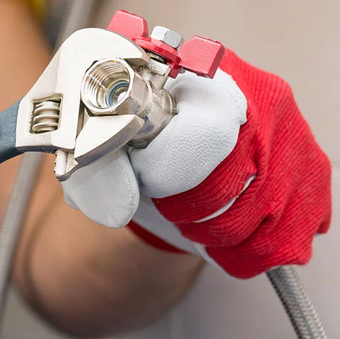 Hand holding an adjustable wrench on a gas valve, emphasizing safety in gas leak situations for HVAC services.
