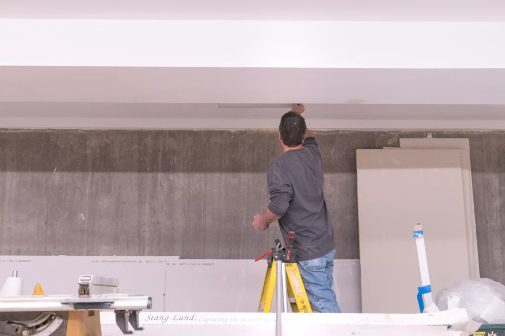 Man working on electrical installation in a residential setting, using a ladder and tools, surrounded by construction materials, emphasizing home renovation services in Mound, MN.