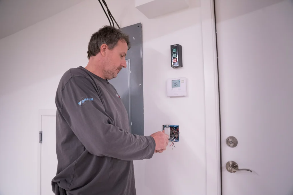 Electrician working on electrical wiring installation, adjusting a thermostat and control panel in a residential setting, highlighting home electrical services in Orono, MN.