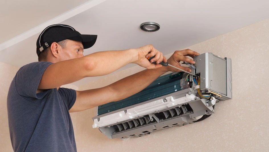 A male technician is working on a ductless mini-split unit attaching a white pipe to the main unit on the wall