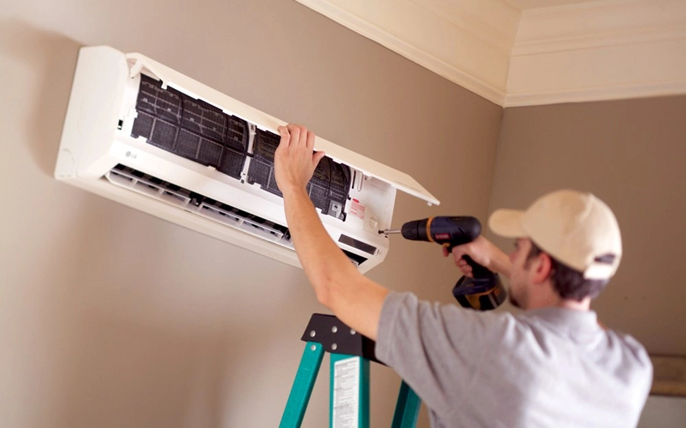Man uses drill on mini-split unit.