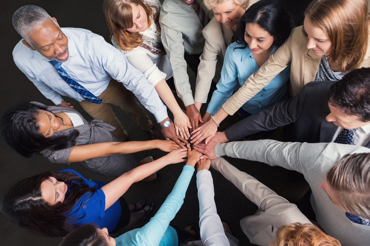 Diverse group of business people standing in a circle with their hands stacked in the center.